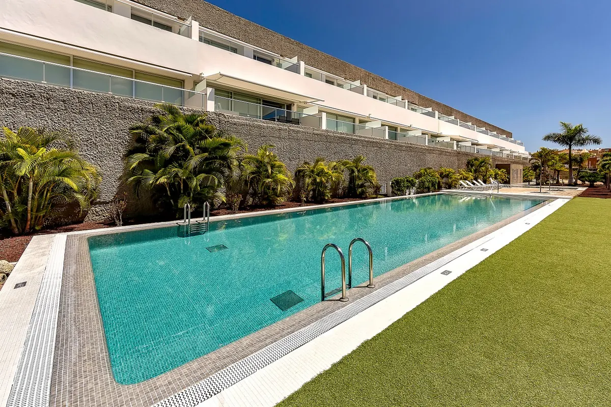 Long communal swimming pool and gardens below a modern apartment building in Tenerife Long communal swimming pool and gardens below a modern apartment building in Tenerife