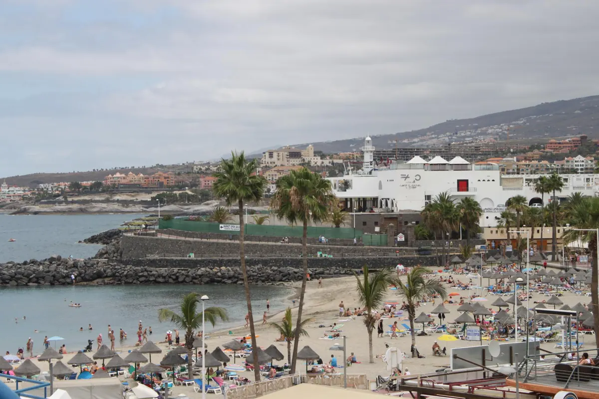 Busy beach with parasols, palm trees and a harbour wall in south Tenerife